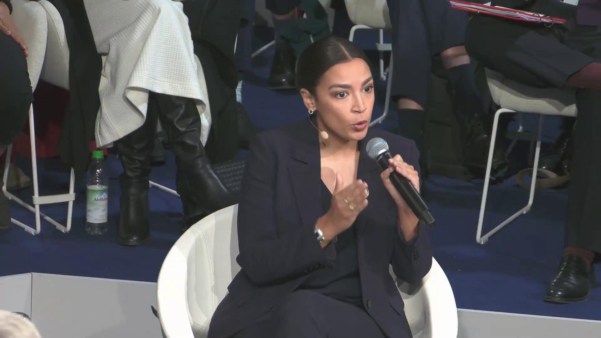 a woman in a black suit sitting on a chair aoc alexandria ocasio cortez alexandria ocasio cortez alexandria ocasiocortez imet2020 extremely clear and coherent film still from dune 2020 sharp and coherent beautiful coherent professional power pose more coherent deepfake joe biden screaming