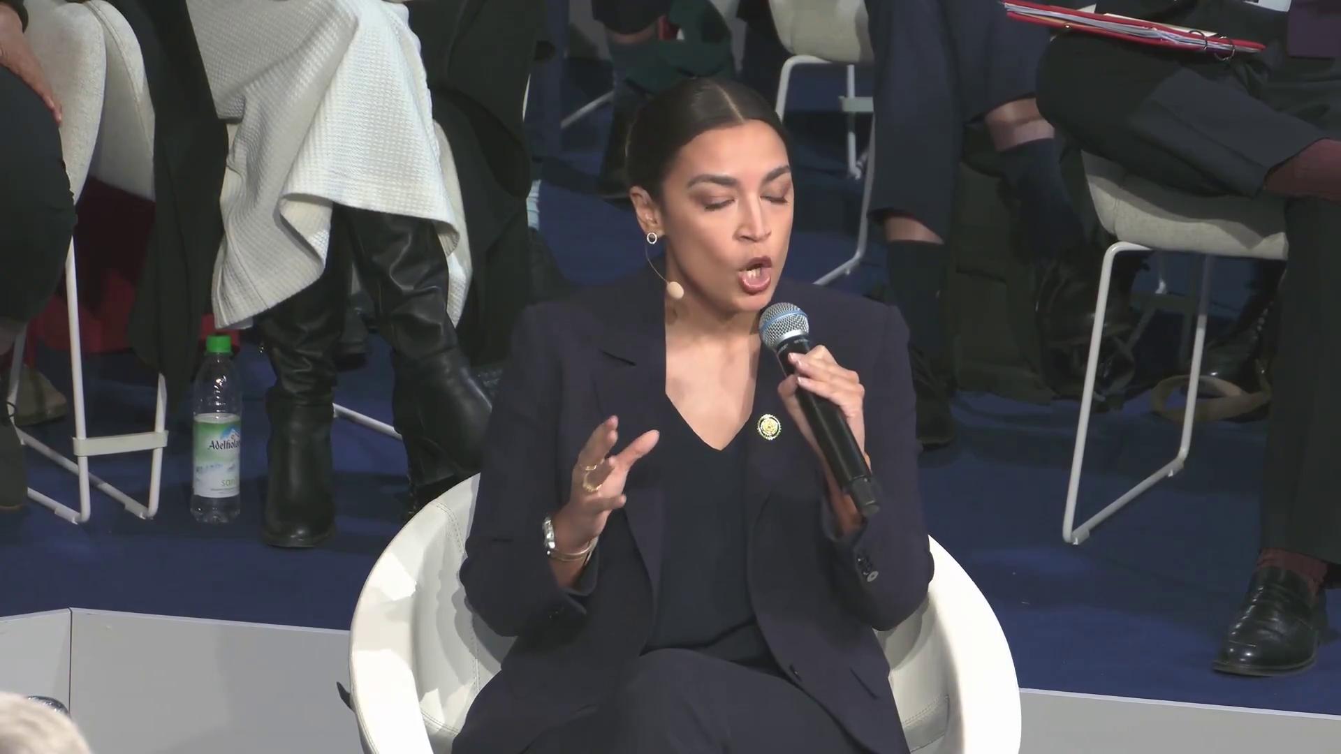a woman in a suit sitting on a chair aoc alexandria ocasio cortez alexandria ocasio cortez alexandria ocasiocortez imet2020 sharp and coherent film still from dune 2020 extremely clear and coherent beautiful coherent professional as a panel of a marvel comic 30yearold woman from cuba