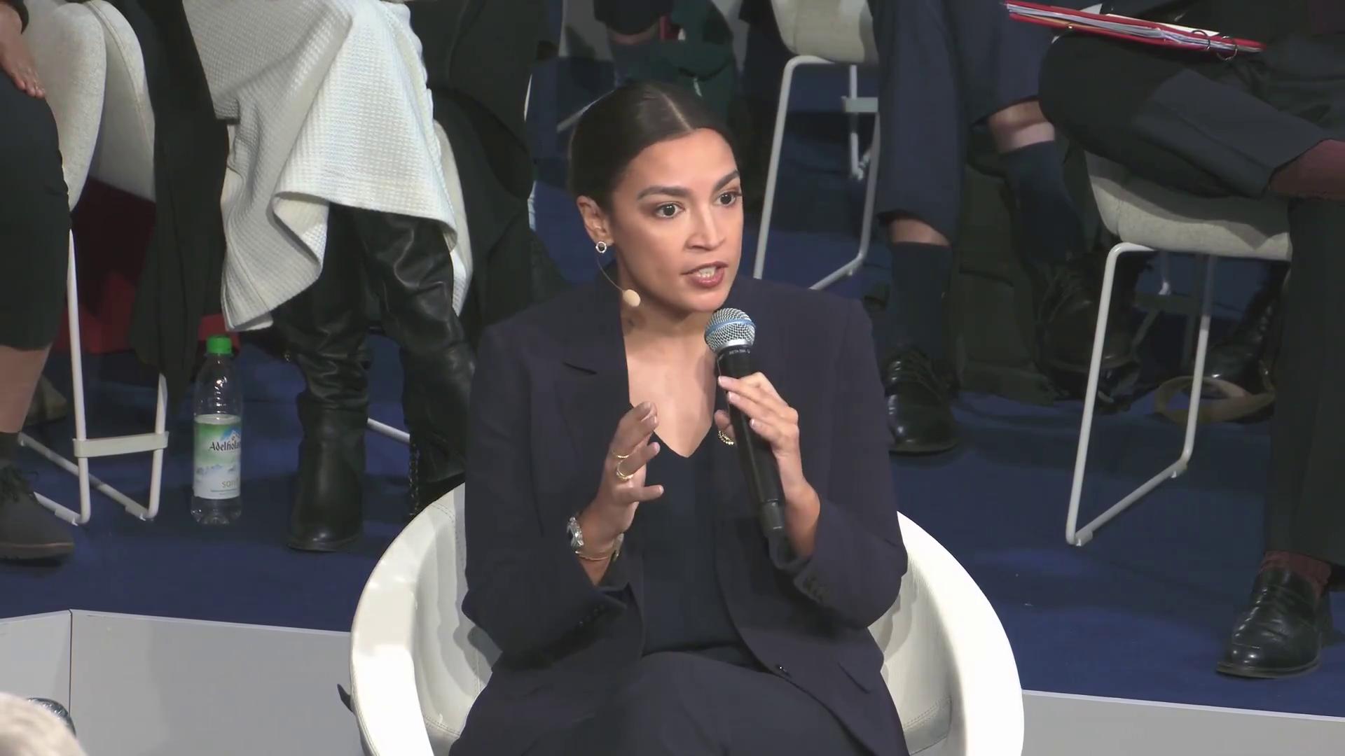 a woman in a suit sitting on a chair alexandria ocasio cortez alexandria ocasio cortez alexandria ocasiocortez aoc imet2020 film still from dune 2020 sharp and coherent extremely clear and coherent beautiful coherent professional film still from movie dune2021 totalitarian socialist angel