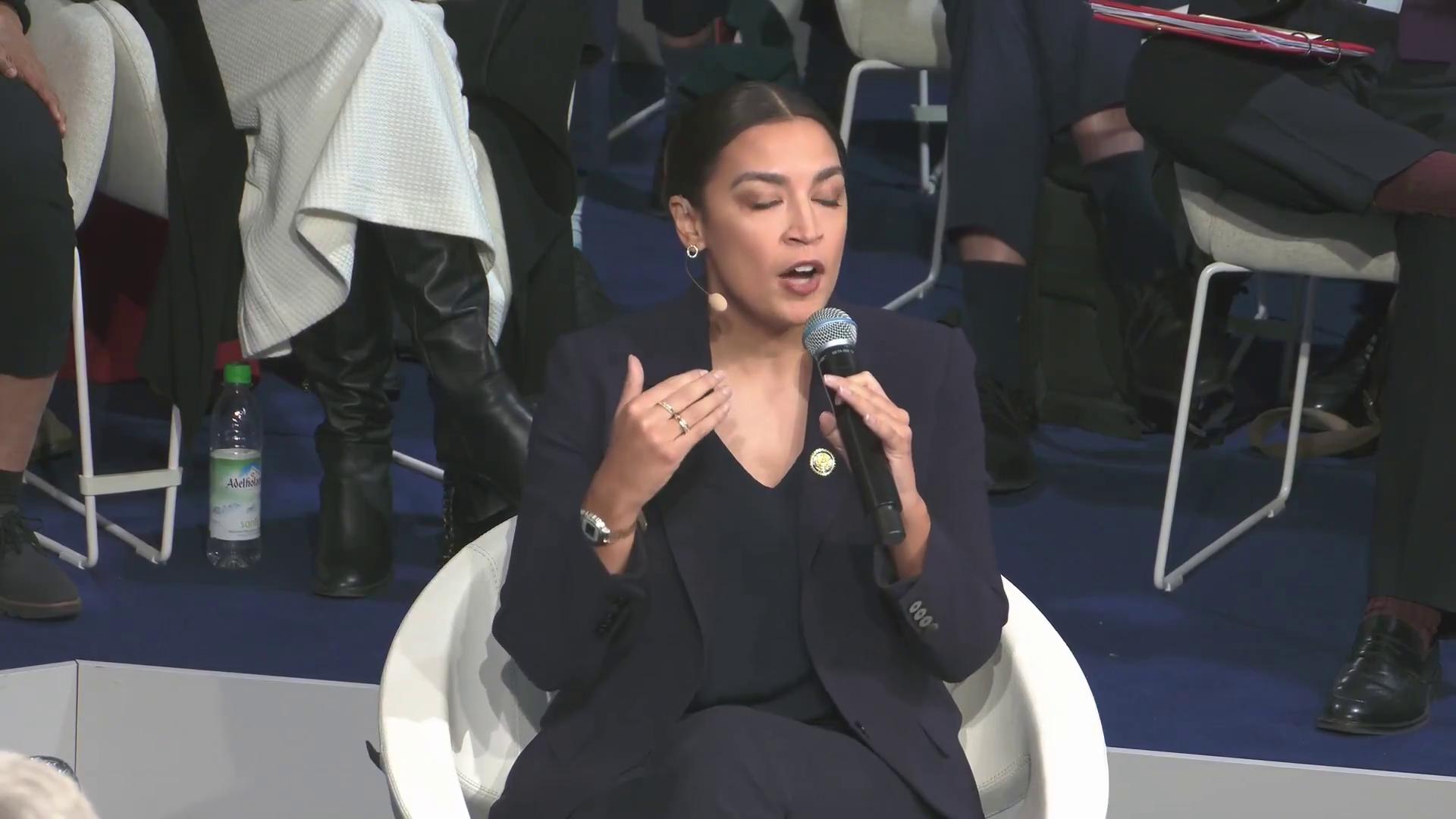 a woman sitting in a chair aoc alexandria ocasio cortez alexandria ocasiocortez alexandria ocasio cortez film still from dune 2020 extremely clear and coherent imet2020 sharp and coherent beautiful coherent professional totalitarian socialist angel deepfake power pose alexandrias genesis more coherent