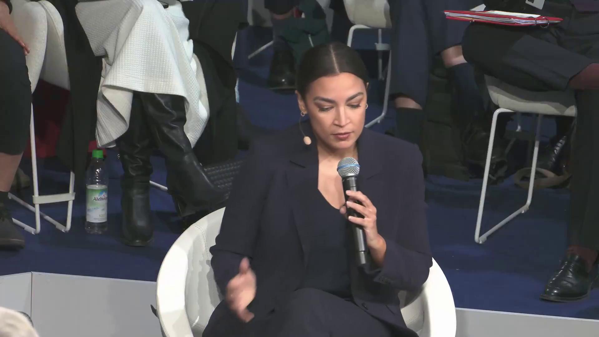 a woman sitting in a chair holding a microphone alexandria ocasio cortez aoc sharp and coherent alexandria ocasio cortez alexandria ocasiocortez beautiful coherent professional extremely clear and coherent imet2020 as a panel of a marvel comic film still from dune 2020 more coherent coherent professional power pose