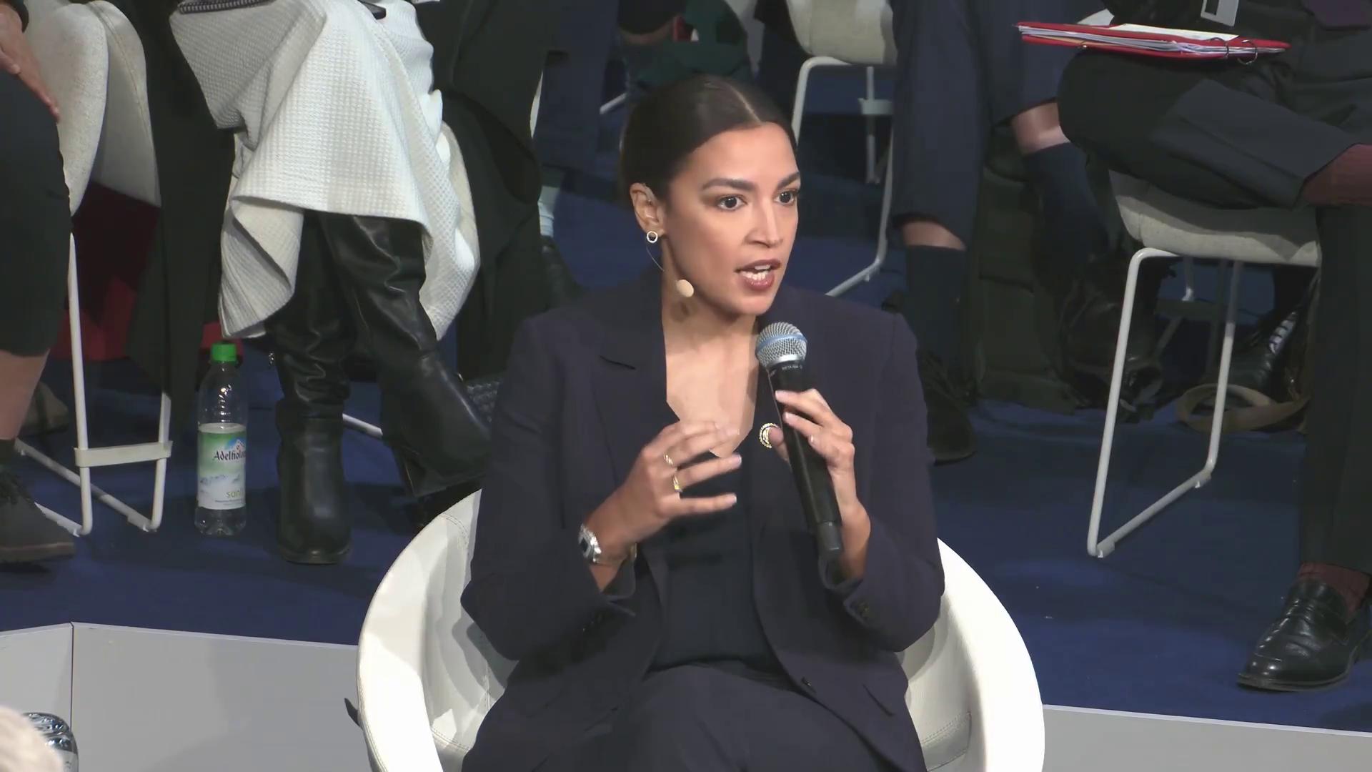 a woman sitting in a chair holding a microphone aoc alexandria ocasio cortez alexandria ocasio cortez alexandria ocasiocortez imet2020 sharp and coherent film still from dune 2020 extremely clear and coherent beautiful coherent professional 30yearold woman from cuba socialist totalitarian socialist angel